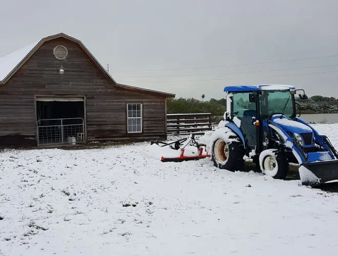 A tractor parked in the snow near a barn.